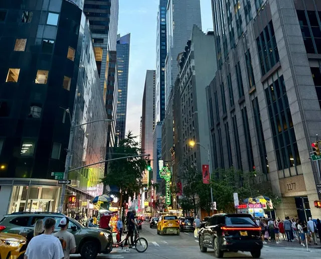 A bustling New York City street at dusk, with office buildings, a yellow taxi, a bicycle courier, and Connolly’s Pub.